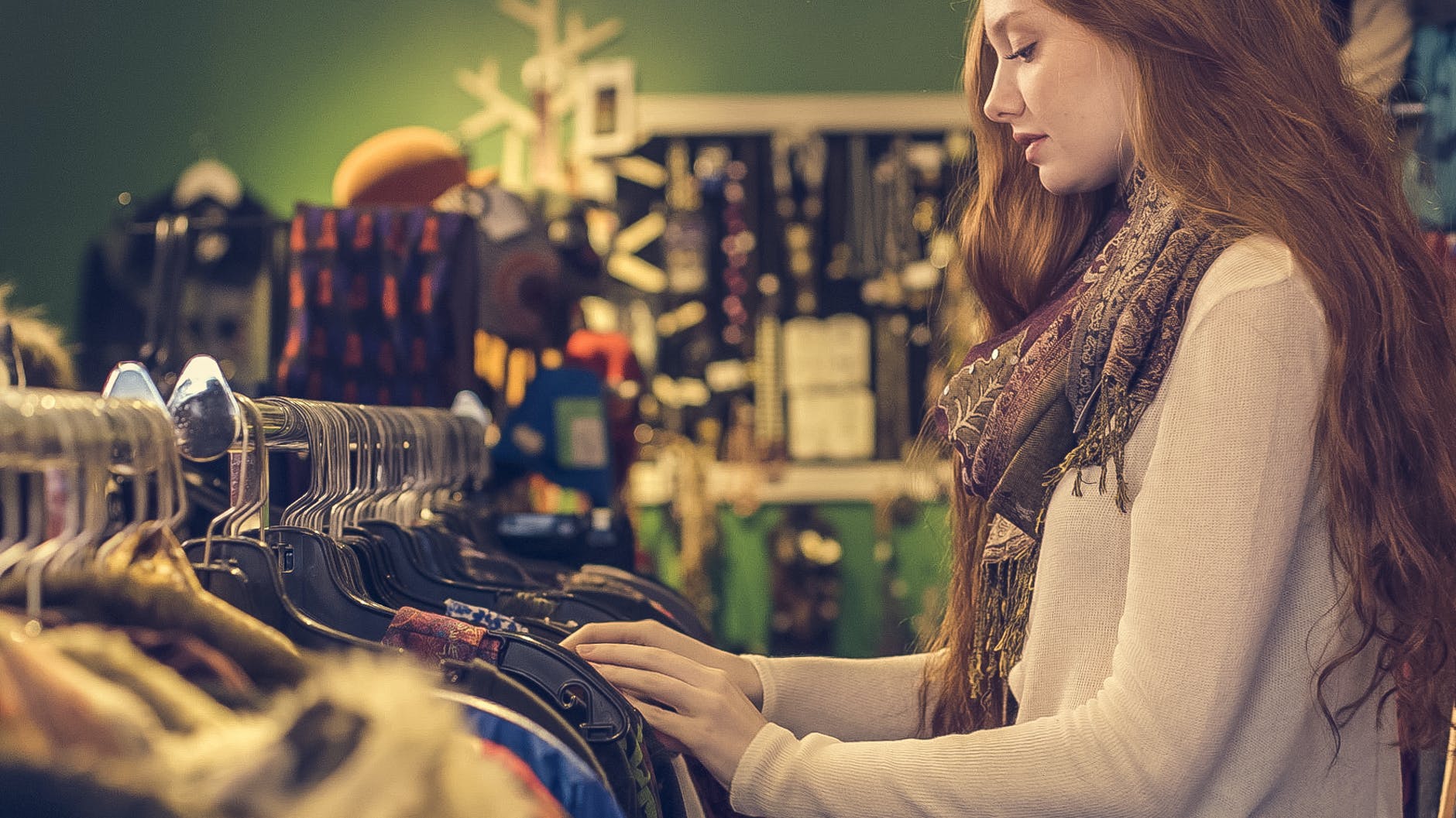 woman wearing white long sleeved shirt with scarf standing near clothes sold in second-hand store for slow fashion